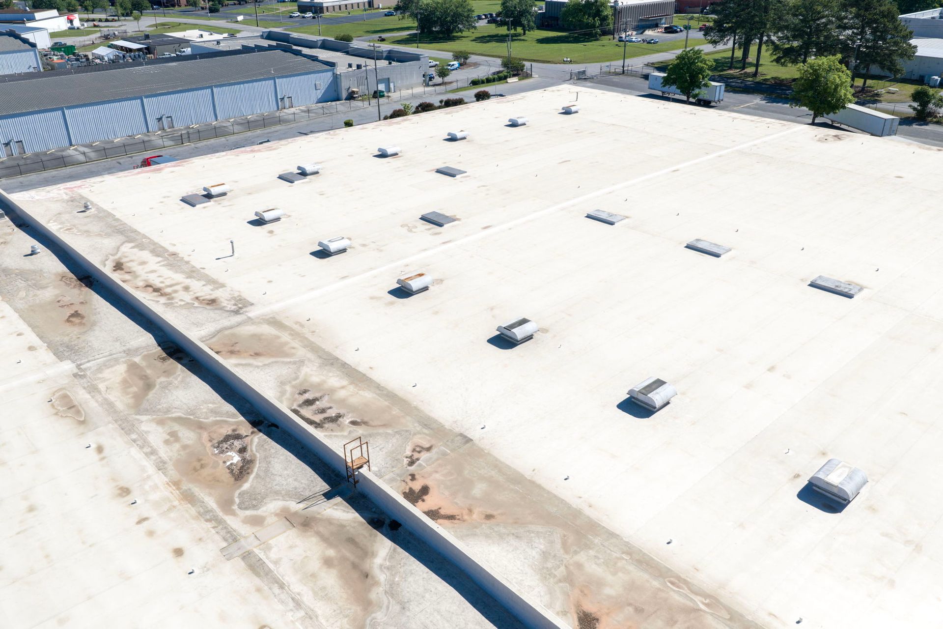 Aerial view of a large white industrial rooftop with vents and nearby buildings.