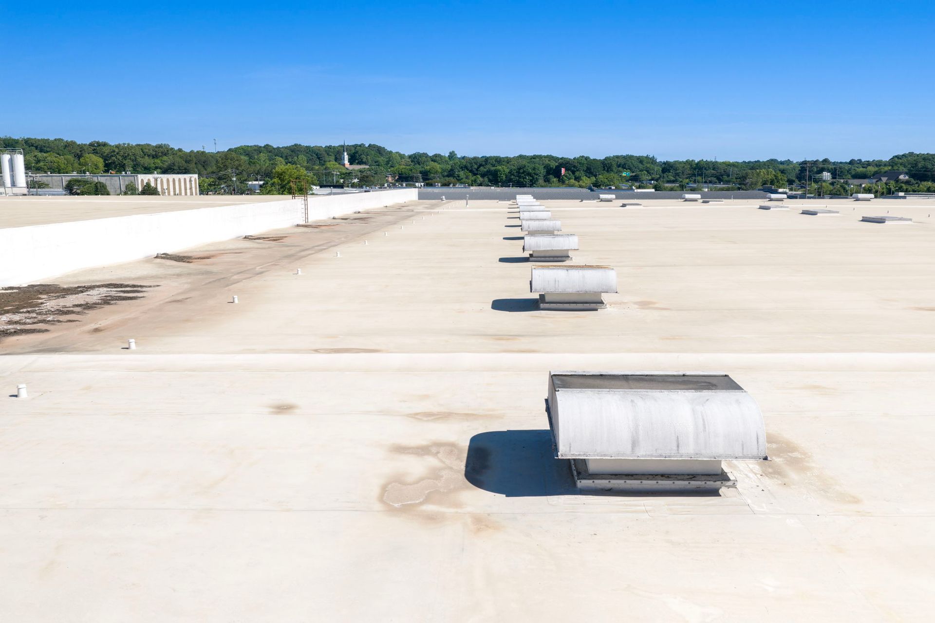 Flat white rooftop with several silver ventilation units under a clear blue sky