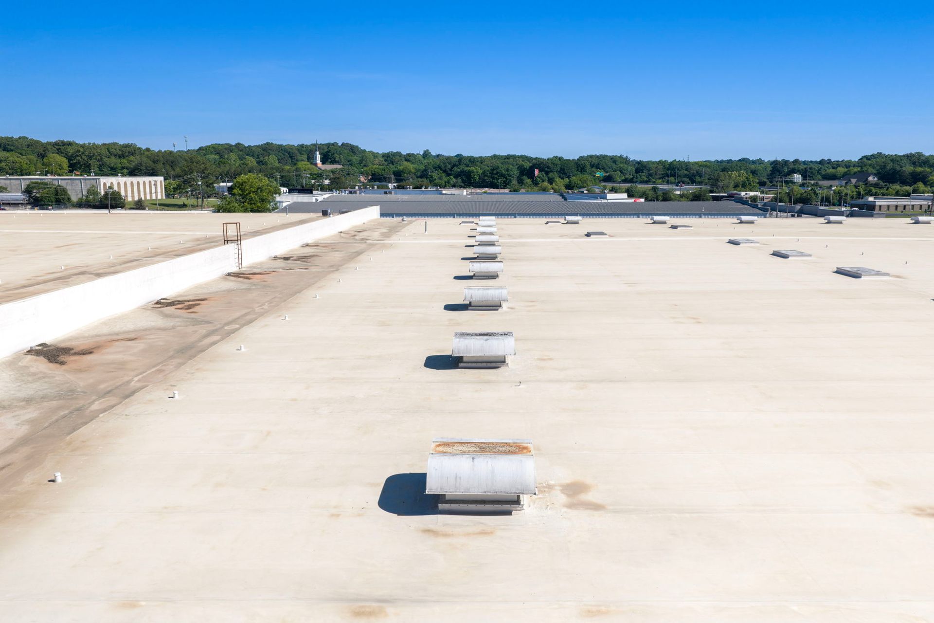 Rooftop with rows of white vents under a clear blue sky, trees in the distance