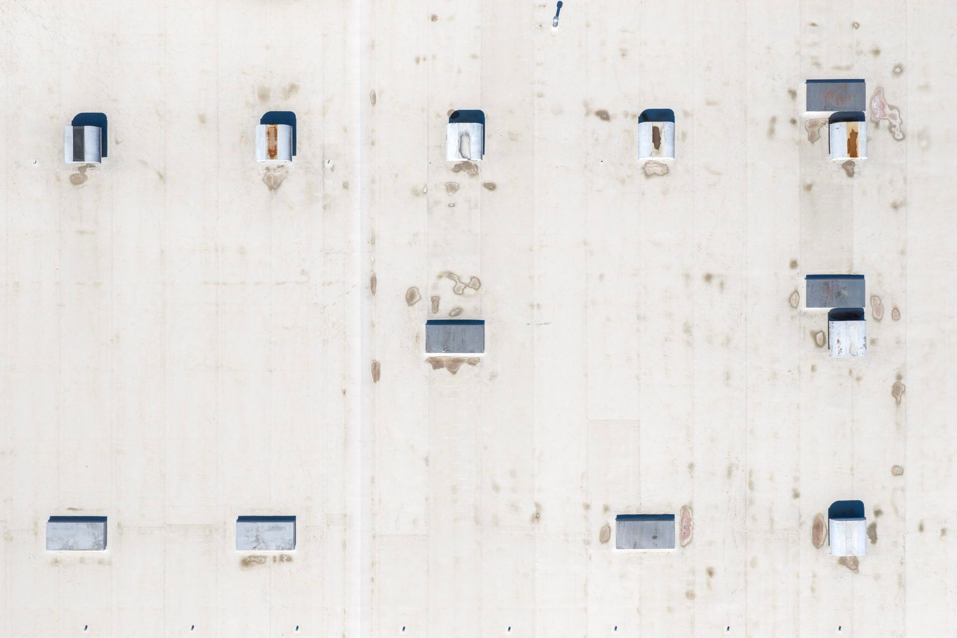 White wall with several small windows and vents, some open, on a building exterior