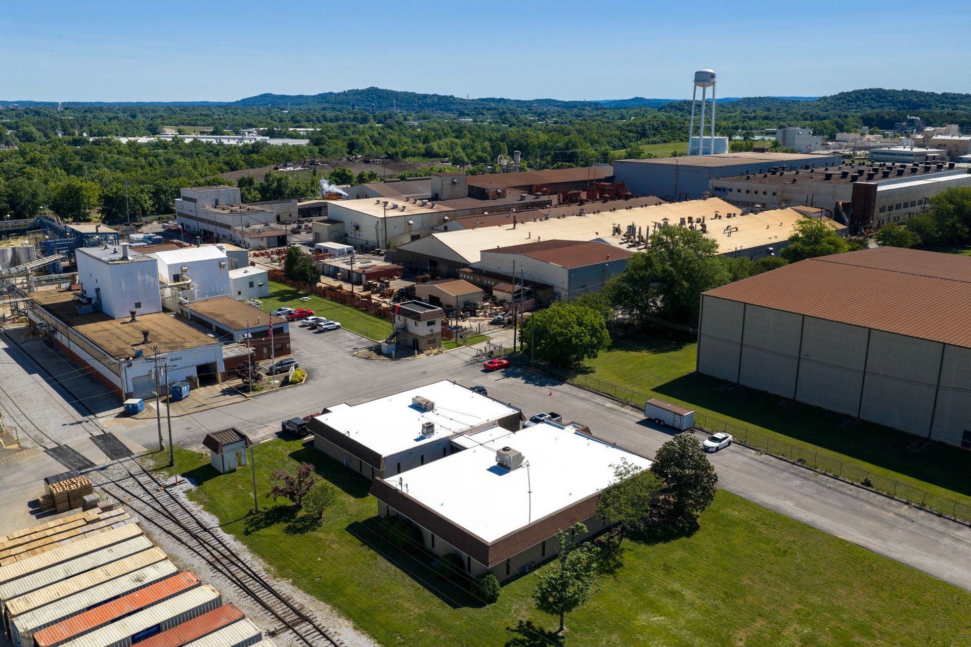 Aerial view of an industrial area with warehouses, roads, and trees under a clear sky