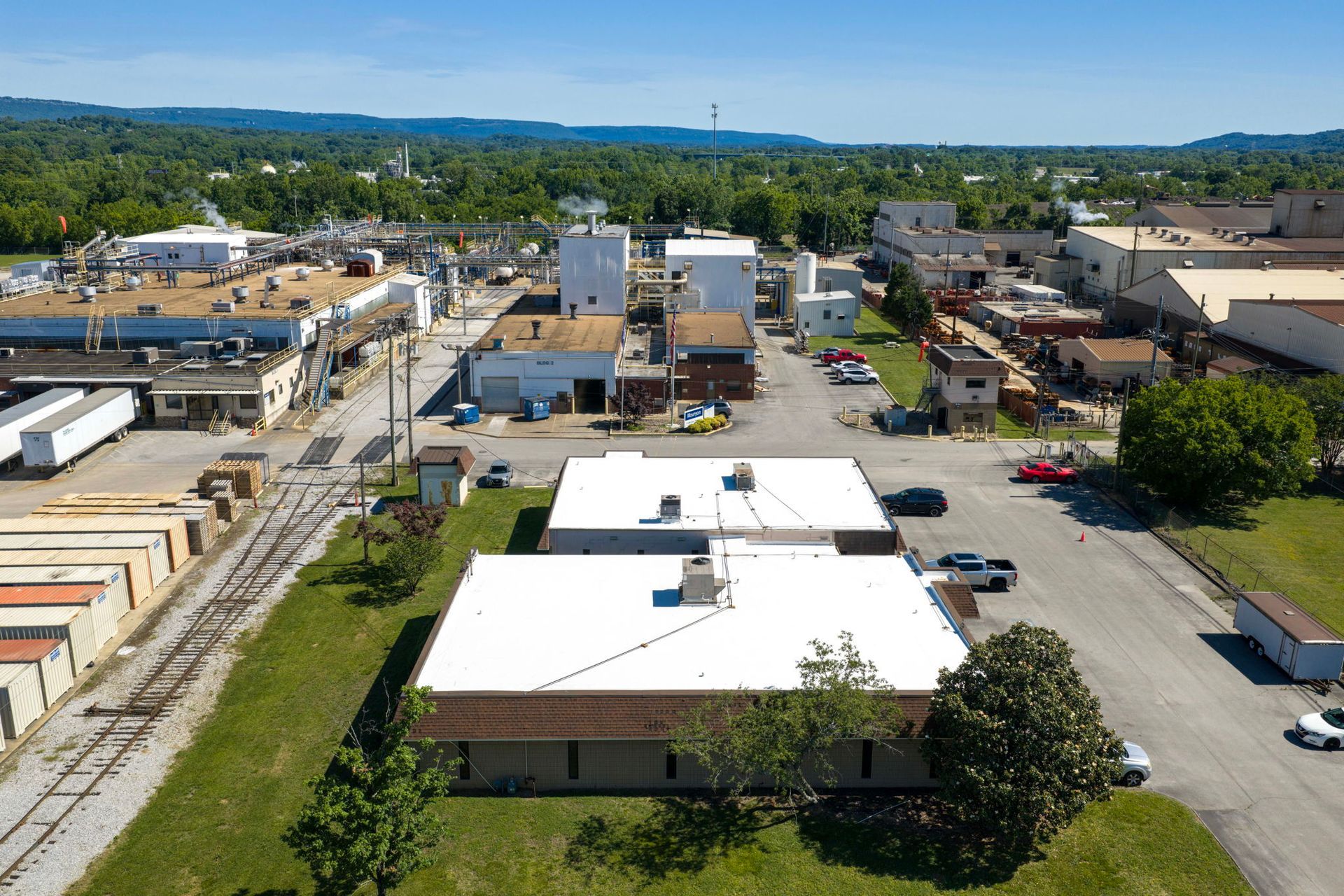 Aerial view of a small town with buildings, parking lots, roads, and trees under a clear sky