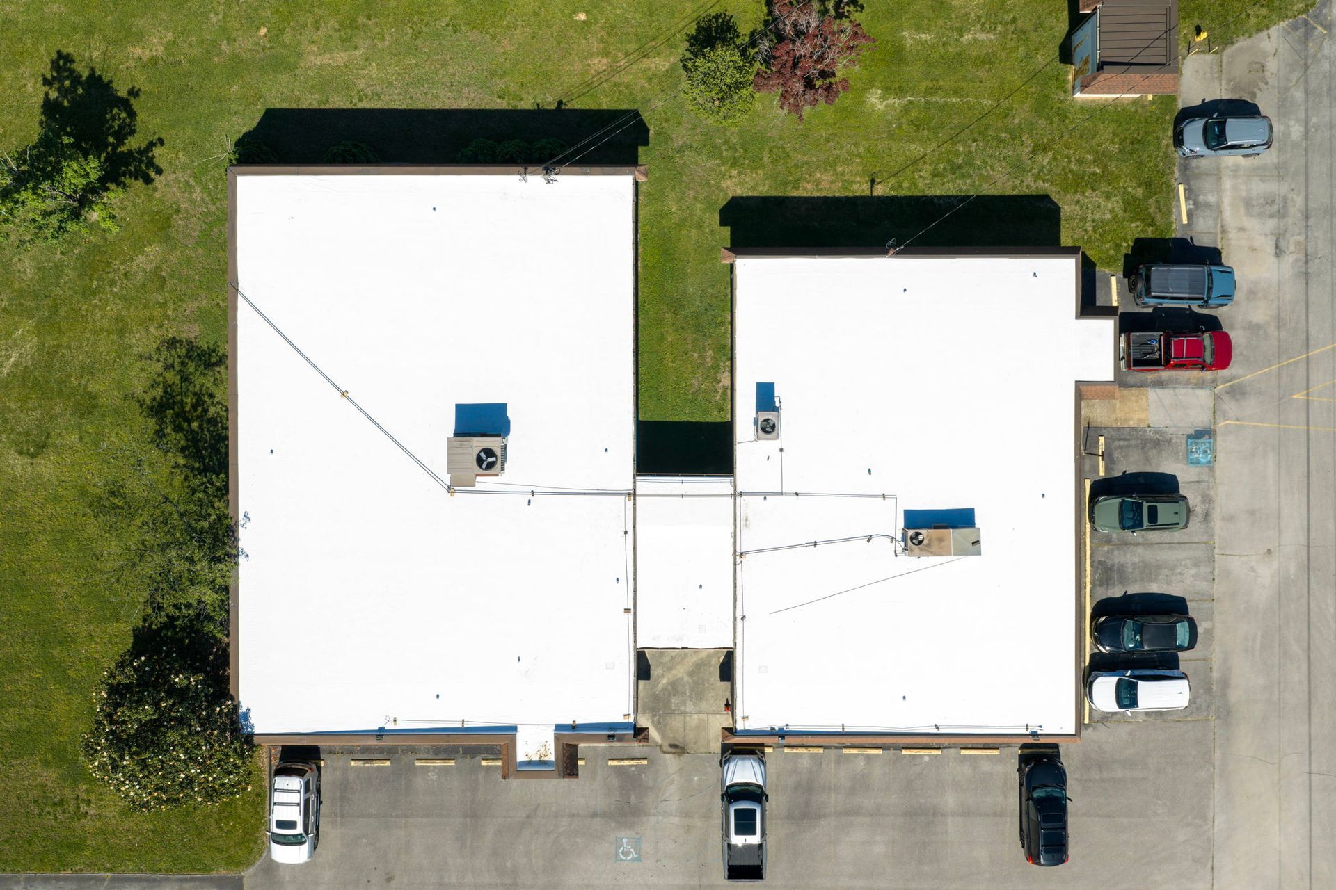 Aerial view of two white buildings with parked cars and grass around them.