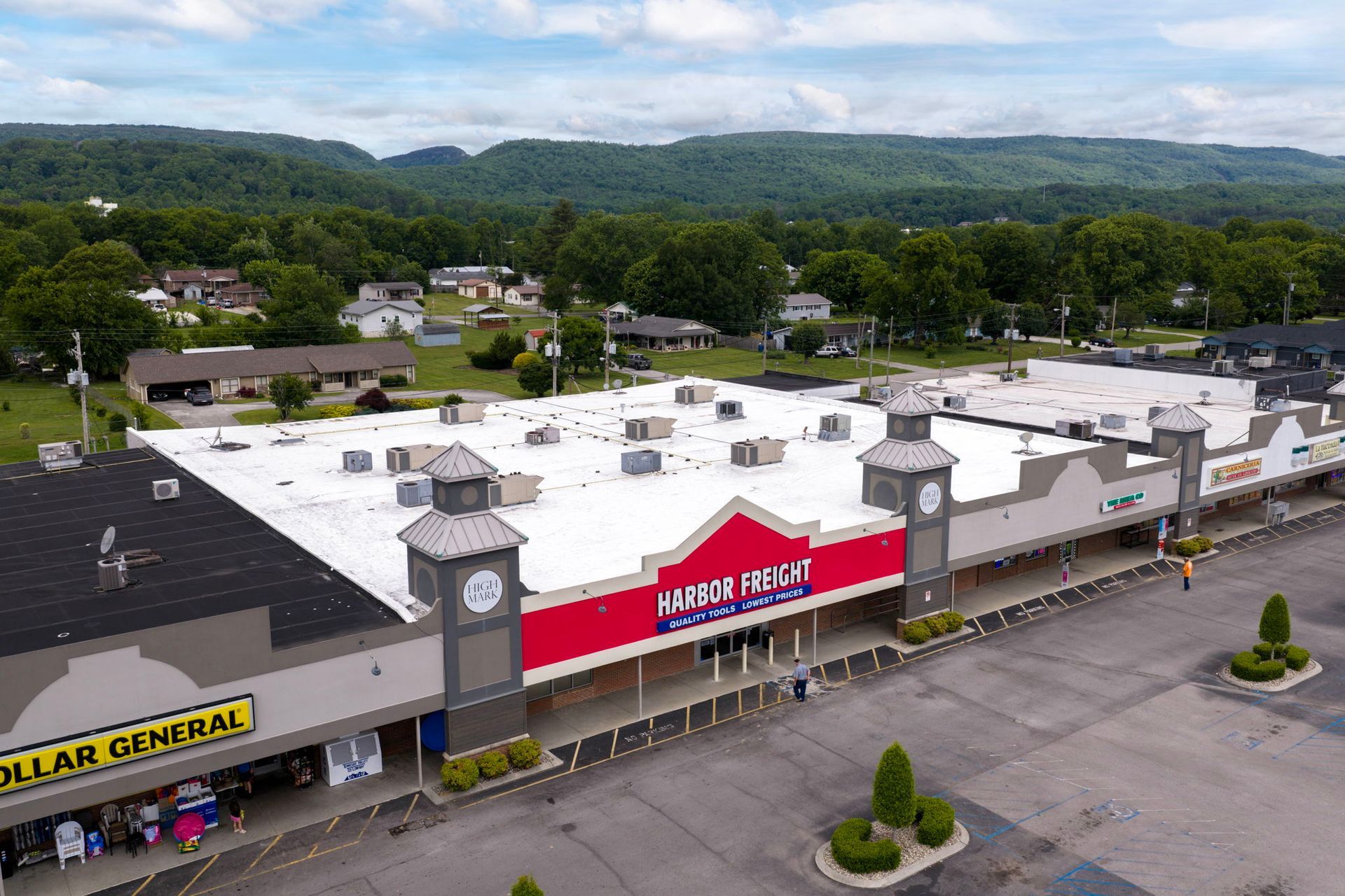 Aerial view of a strip mall with a clock tower, white roofs, and mountains in the background