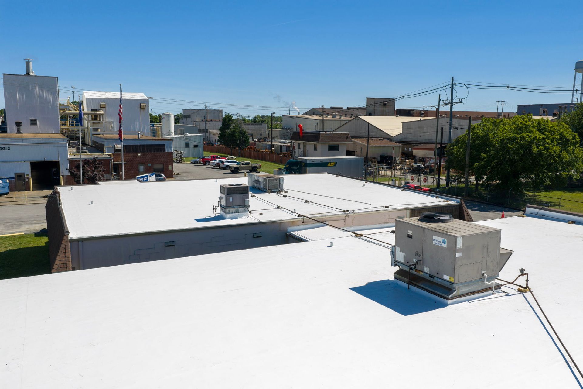 Rooftop with white surface, HVAC units, and a city street skyline under a clear blue sky
