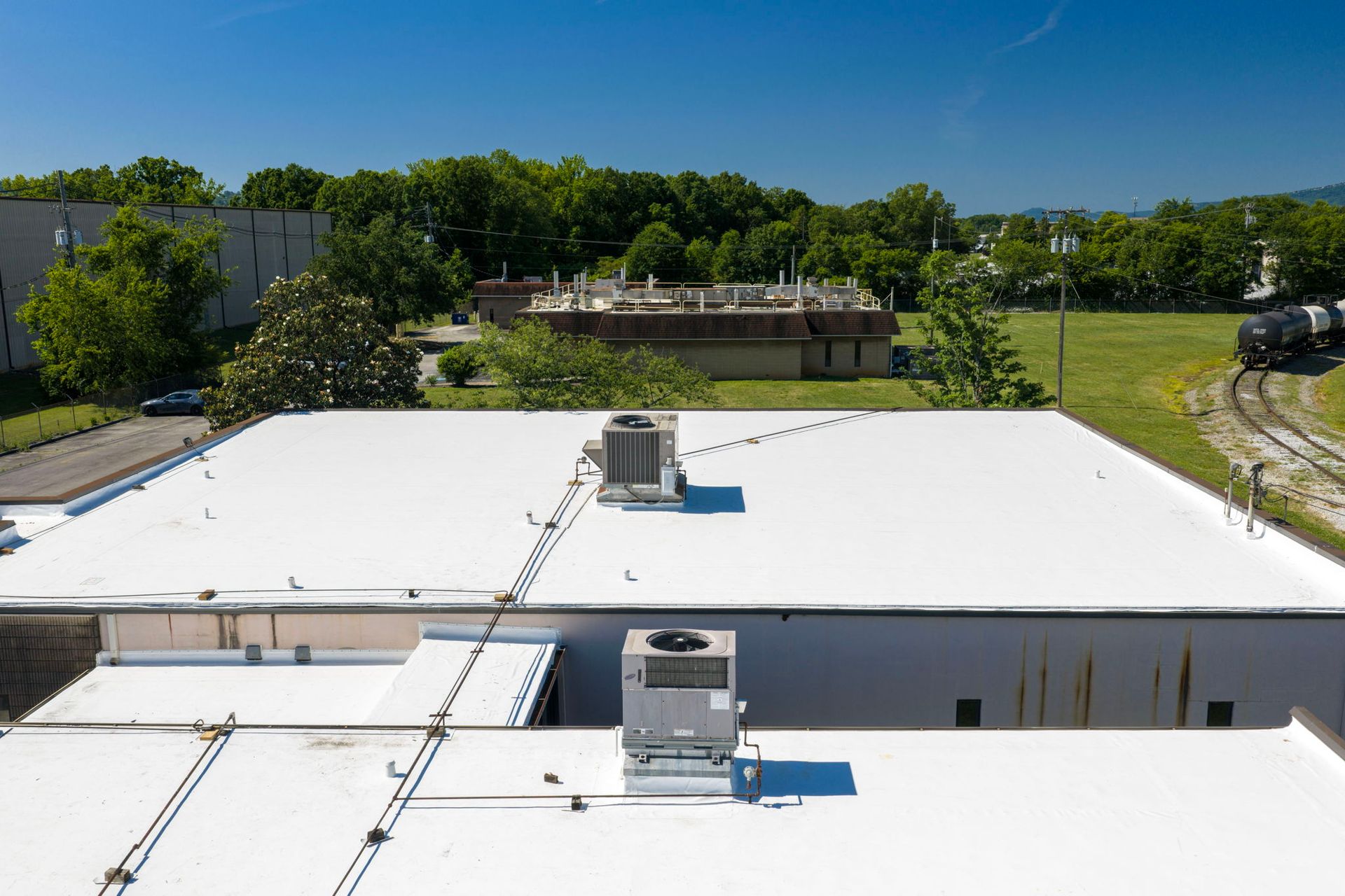 Flat white rooftop with HVAC units, trees and a blue sky in the background