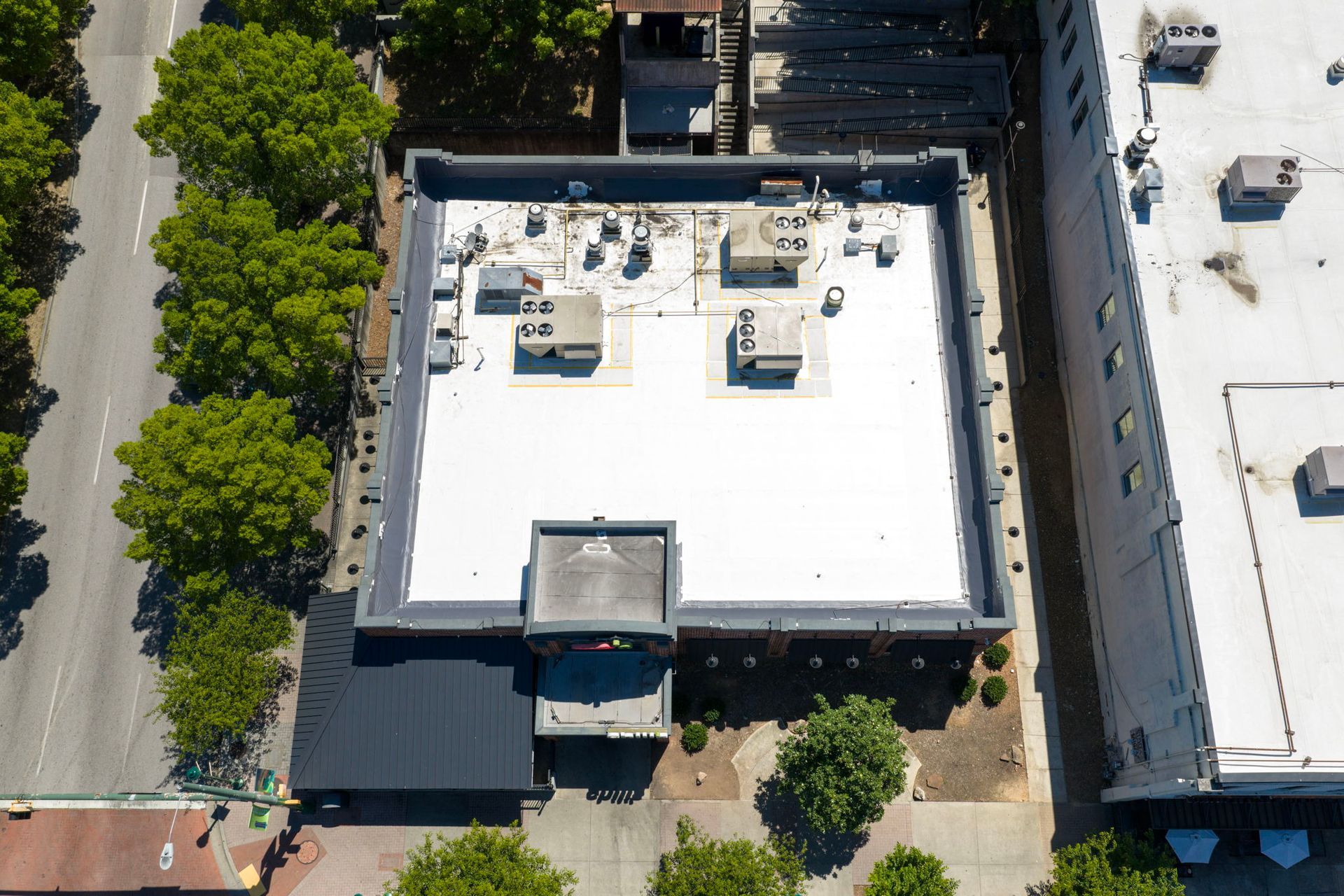 Aerial view of a flat-roofed building with trees and sidewalks along the street