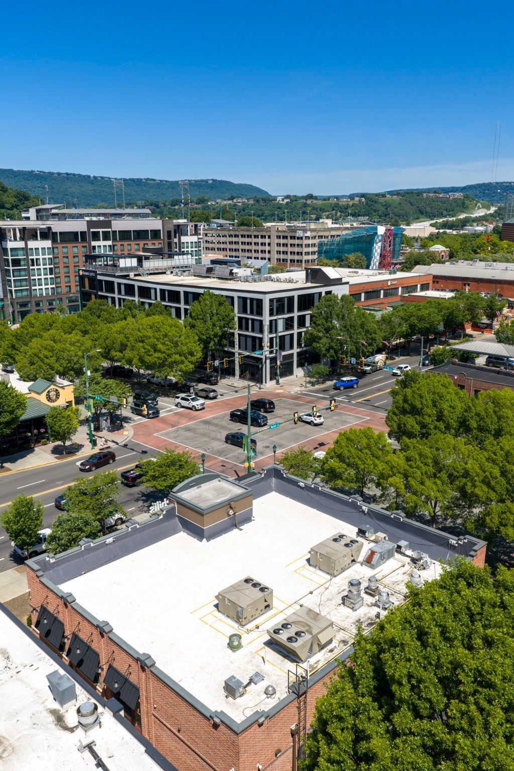 Downtown cityscape with mid-rise buildings, a busy intersection, and trees under a clear blue sky