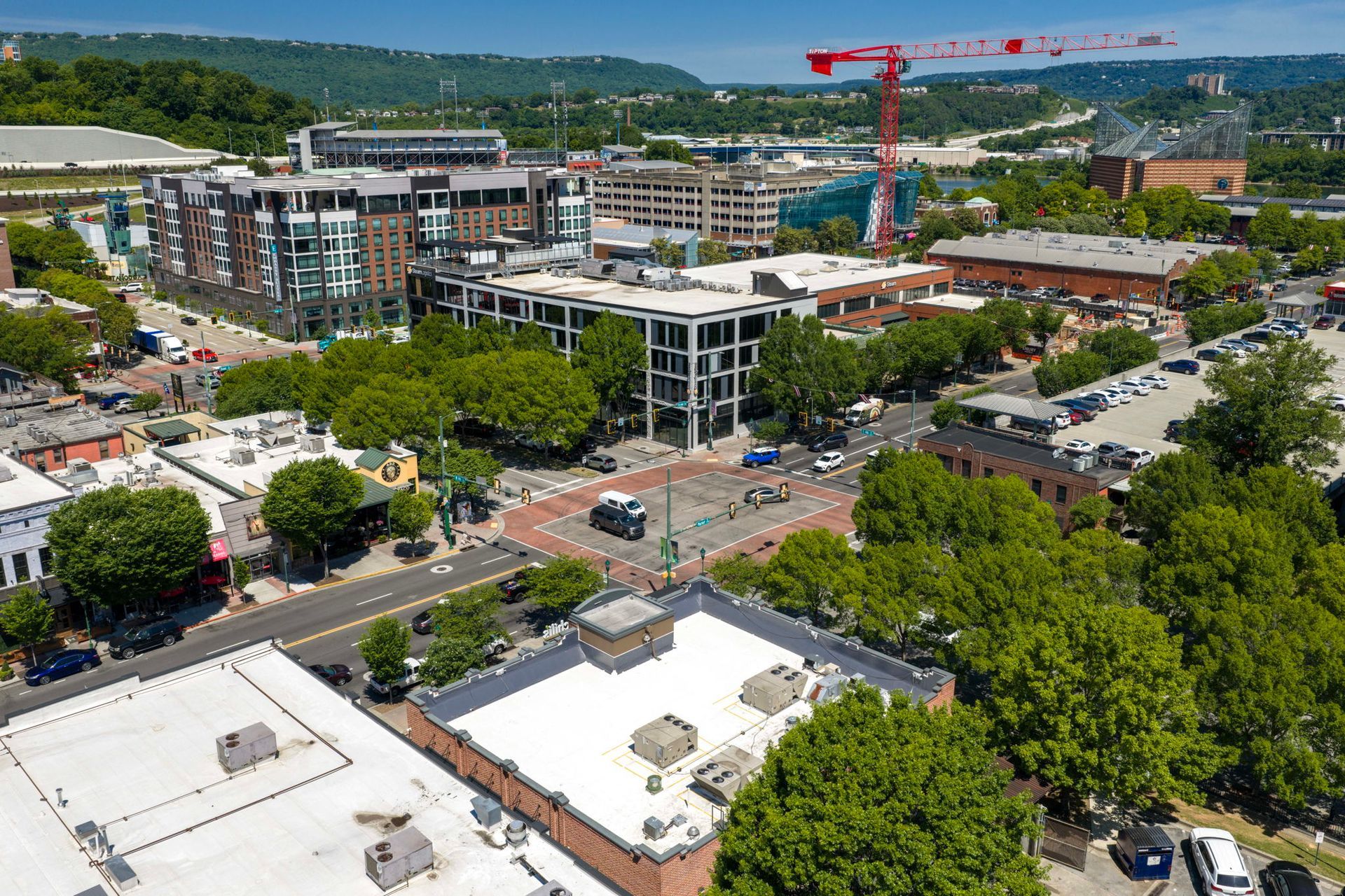 Aerial view of a city center with buildings, trees, traffic, and a red construction crane under a clear sky