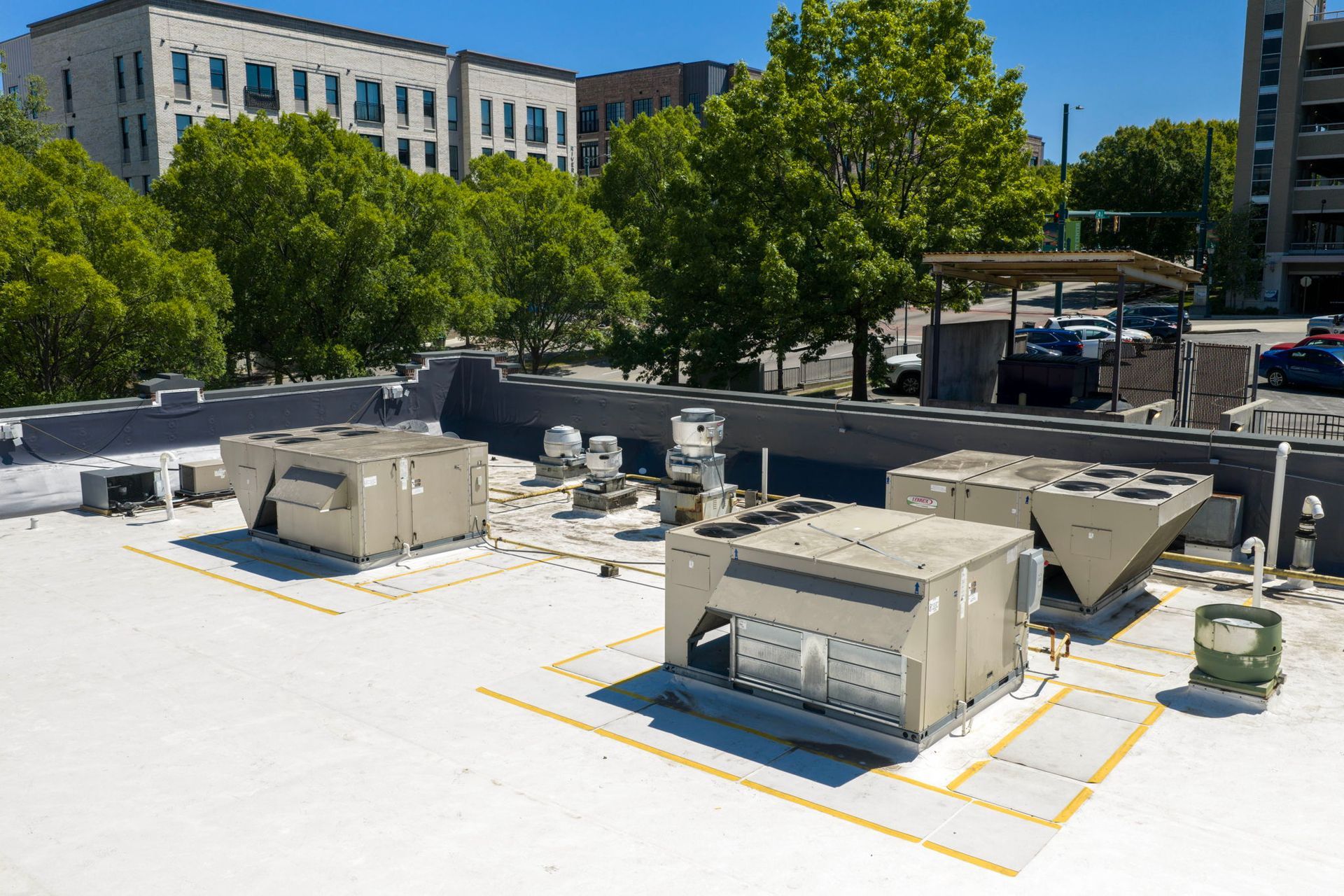 Rooftop HVAC units on a white commercial roof with trees and office buildings in the background