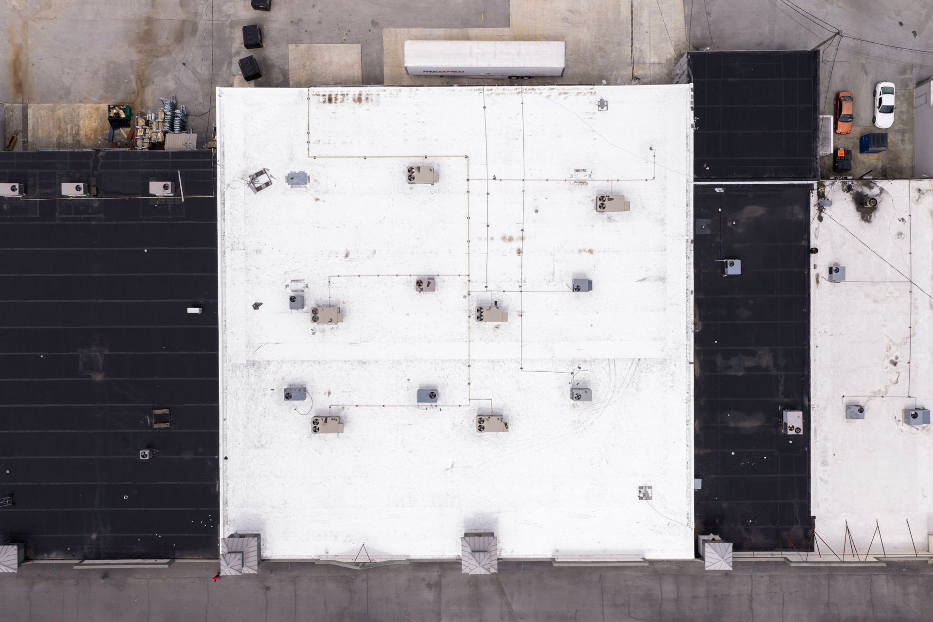 Aerial view of flat rooftops: one white center roof between two dark roofs, with HVAC units and vents.