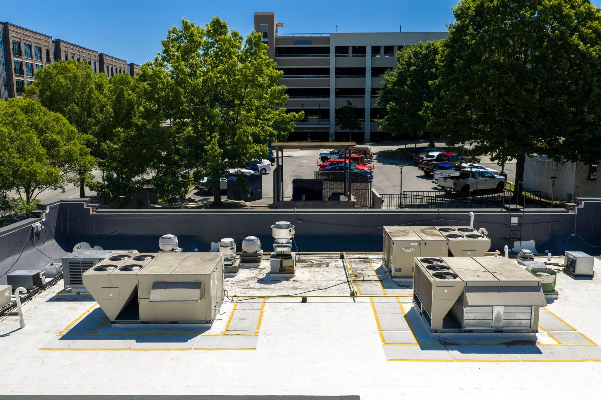 Rooftop HVAC units and vents overlooking a parking lot and mid-rise buildings under trees