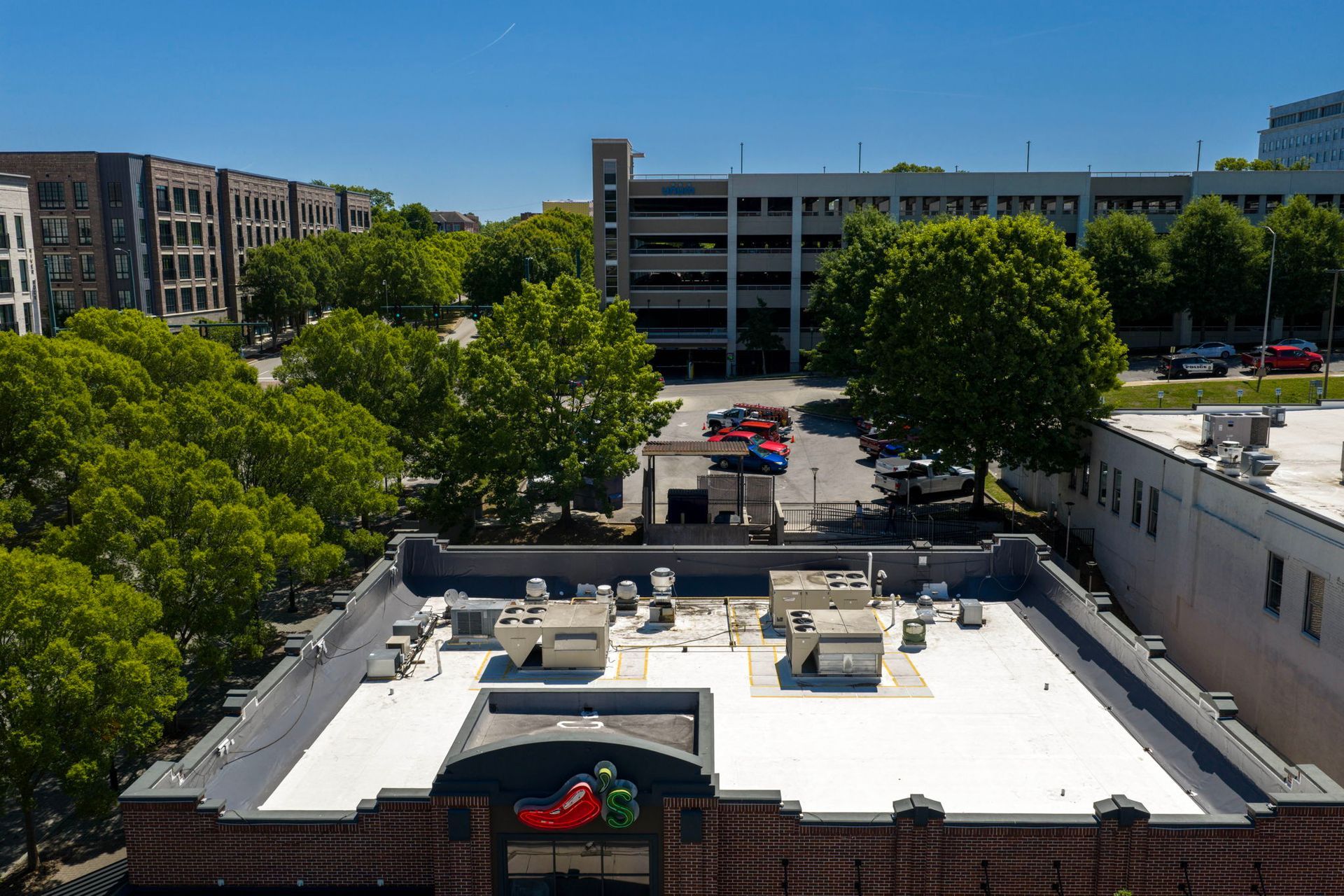 Urban rooftop view with white roof, trees, parking lot, and buildings under a blue sky