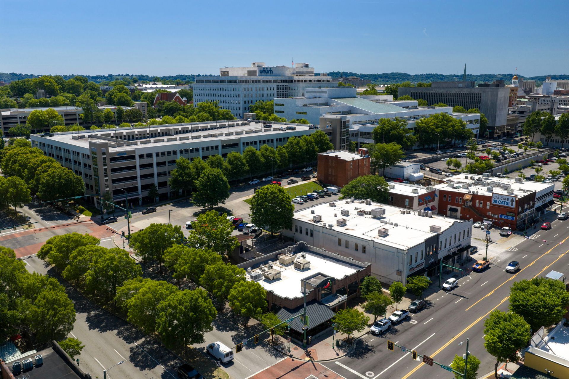 Aerial view of a downtown area with buildings, streets, trees, and parked cars under clear skies