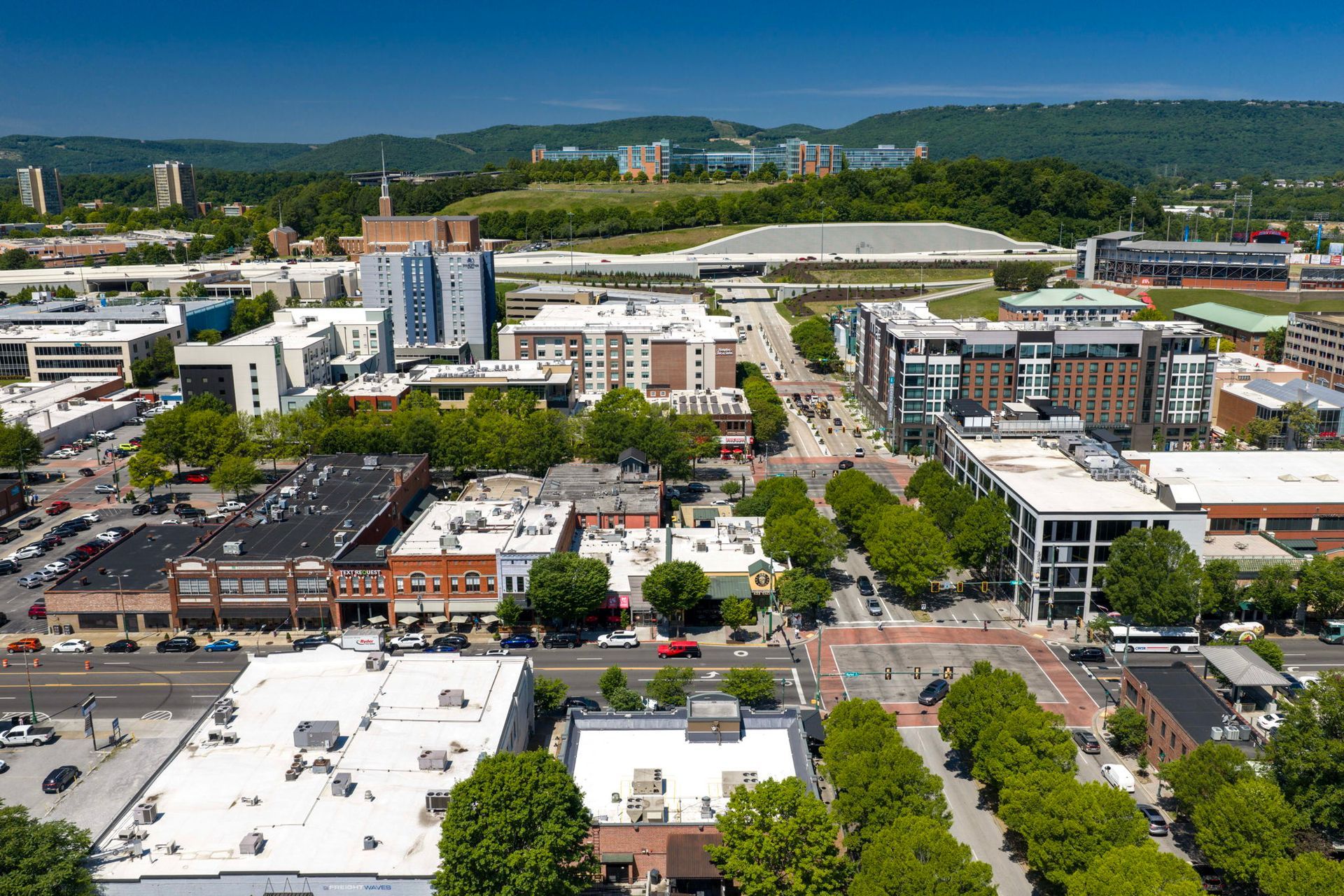 Aerial view of a downtown area with roads, buildings, trees, and hills in the background