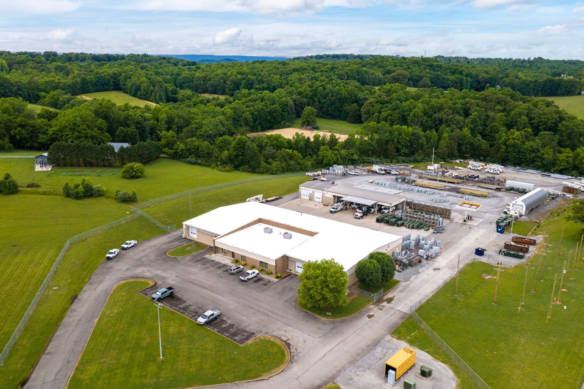 Aerial view of an industrial warehouse complex beside green fields and dense forest.