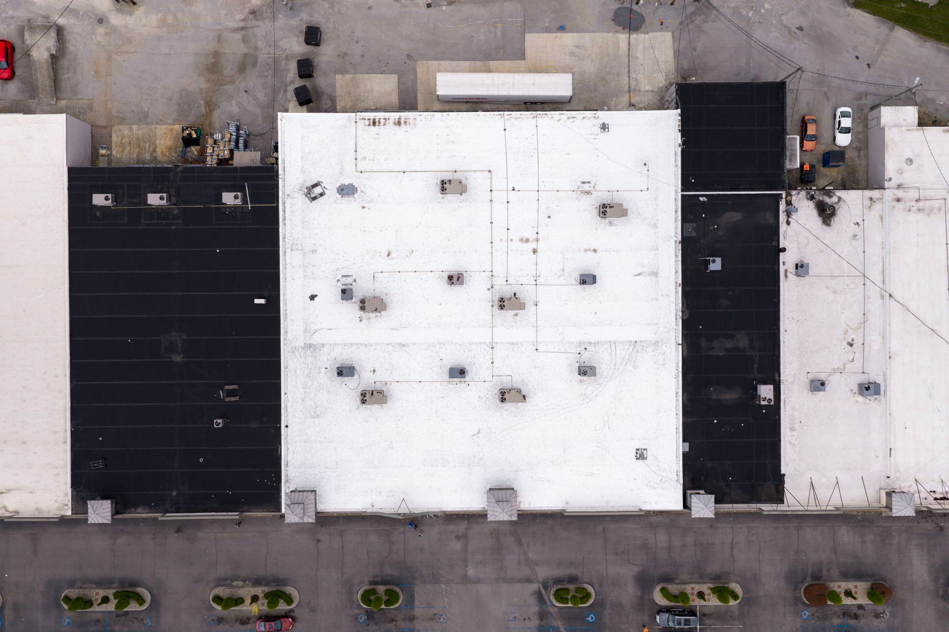 Aerial view of flat-roofed commercial buildings beside a street with parked cars.