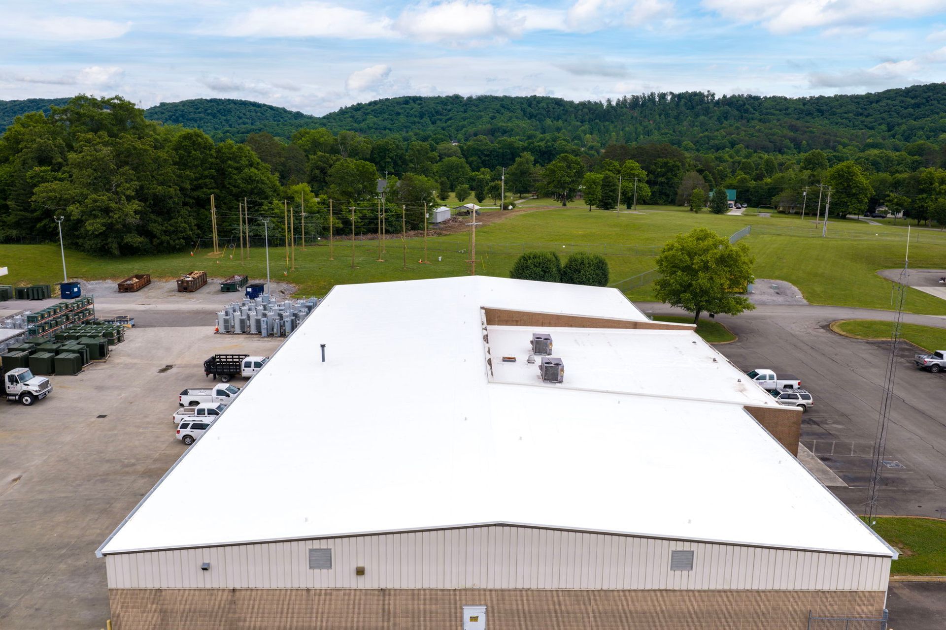 Aerial view of a large white-roofed building with parking lots and trees in the background.
