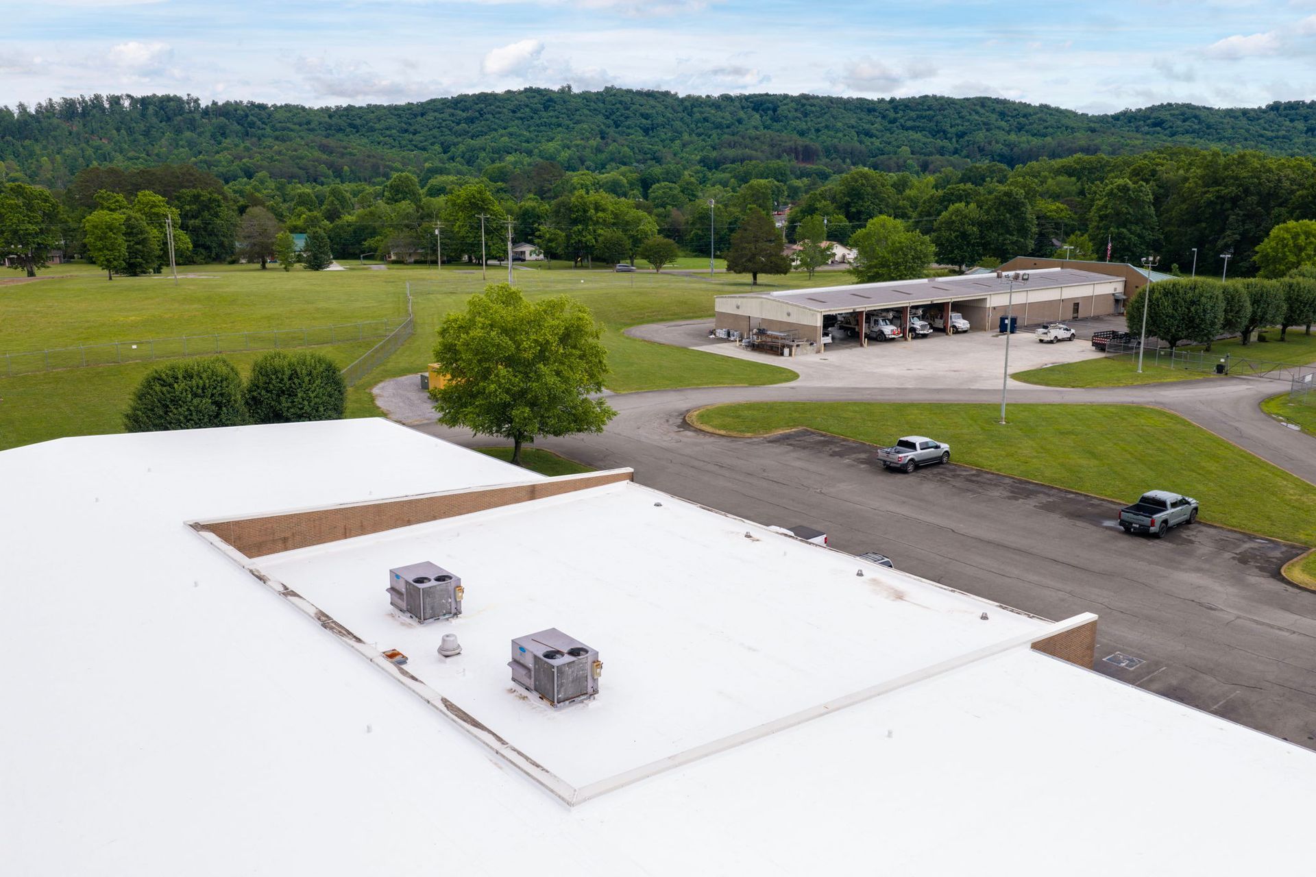 Rooftop with two vents overlooking a parking lot, grassy field, and forested hills