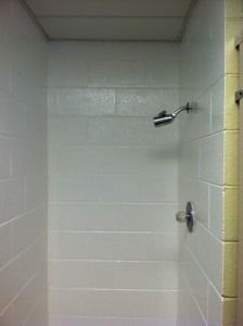 A shower stall featuring white concrete block walls, a chrome showerhead, and a single lever handle on the right.