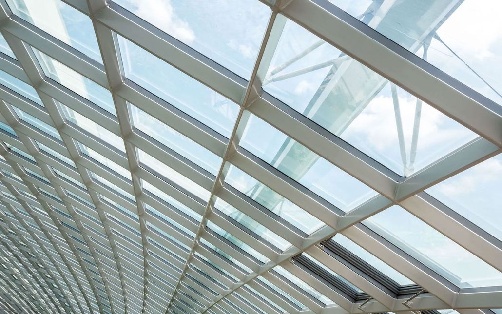 A curved modern glass ceiling with a white metal grid frame against a bright sky.