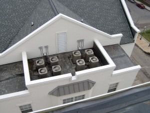 A high-angle view of a white building roof featuring a rectangular area containing eight HVAC units.