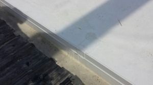 A white surface meets a textured, dark gray edge, divided by a thin light-colored strip, with a long diagonal shadow.