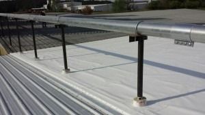 A metallic guardrail system mounted on a white flat roof, featuring vertical supports anchored to the roofing surface.