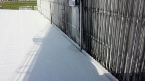 A white flat roof meets a tall, weathered metal wall featuring dark vertical streaks of staining.
