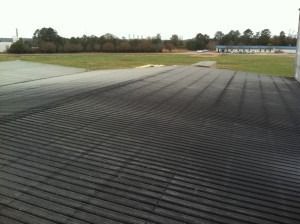 A view from a high vantage point looking down at a large, flat, corrugated black roof leading to an open grassy field.
