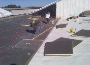 Two construction workers installing insulation panels on a flat commercial roof.
