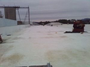 A white, flat roof surface stretches toward the horizon under a cloudy sky, with industrial structures in the distance.