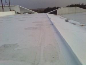 A flat, white roof surface featuring a raised seam or flashing detail, with structural supports visible in the distance.