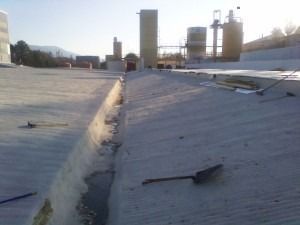 An industrial concrete roof with a central drainage channel and scattered construction tools under a bright sky.