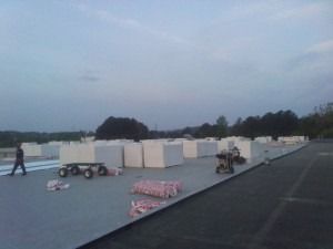 Workers on a flat roof setting out stacks of white insulation boards for a construction project at dusk.
