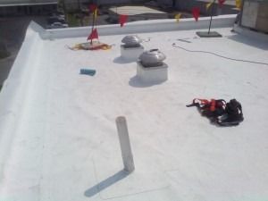 A white flat roof featuring two circular vents, a ventilation pipe, safety flags, and a black equipment bag.