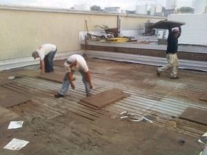 Three workers installing flooring materials on a rooftop.