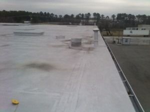 A view from a rooftop looking out over a paved lot with a distant road and trees under an overcast sky.