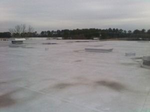 A flat, gray, low-slope commercial roof with several vents and HVAC units under a cloudy sky.