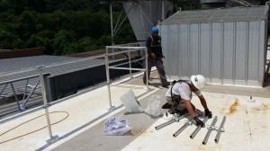 Two construction workers assemble metal framing on a flat, industrial rooftop.
