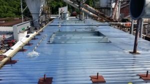 An overhead view of a blue, corrugated metal roof with industrial equipment and structural support beams.