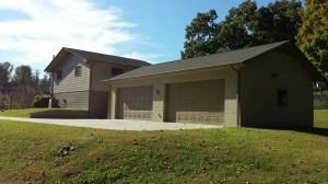 A two-story, grey house with an attached two-car garage sits on a grassy lawn under a clear blue sky.