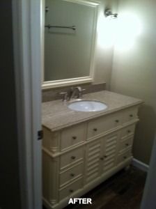 A bathroom vanity with a light-colored cabinet, beige stone countertop, and an oval sink, viewed through a doorway.