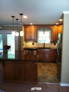 A kitchen with wood cabinets, a black countertop island, three hanging pendant lights, and brown tile flooring.