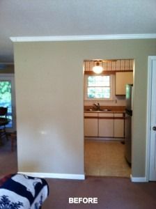 A view of a tan wall with a doorway leading to a kitchen with cabinets, a window, and stainless steel appliances.