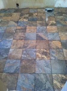 A floor covered in square, multicolored slate tiles in shades of brown, gray, and blue, with a metal vent in the corner.