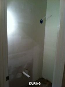 A small, unfinished bathroom renovation with exposed white pipes extending from a wall patched with drywall compound.