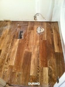 New wood flooring partially installed in a room with a floor vent and plumbing pipe visible. The label says DURING.