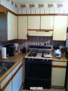 A kitchen with tan laminate countertops, off-white cabinets with wood trim, and floral wallpaper labeled 