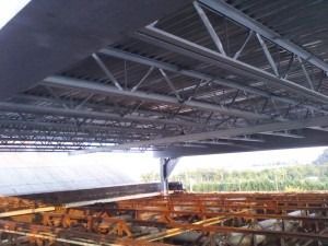 Steel trusses and metal decking supporting the underside of a large building structure, with construction materials below.